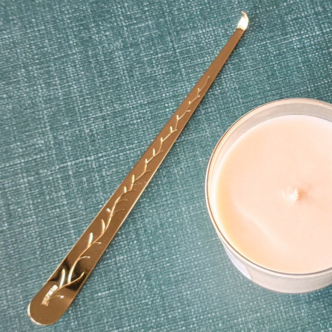 Gold-colored metal tool with engraved design next to a candle on a textured green surface