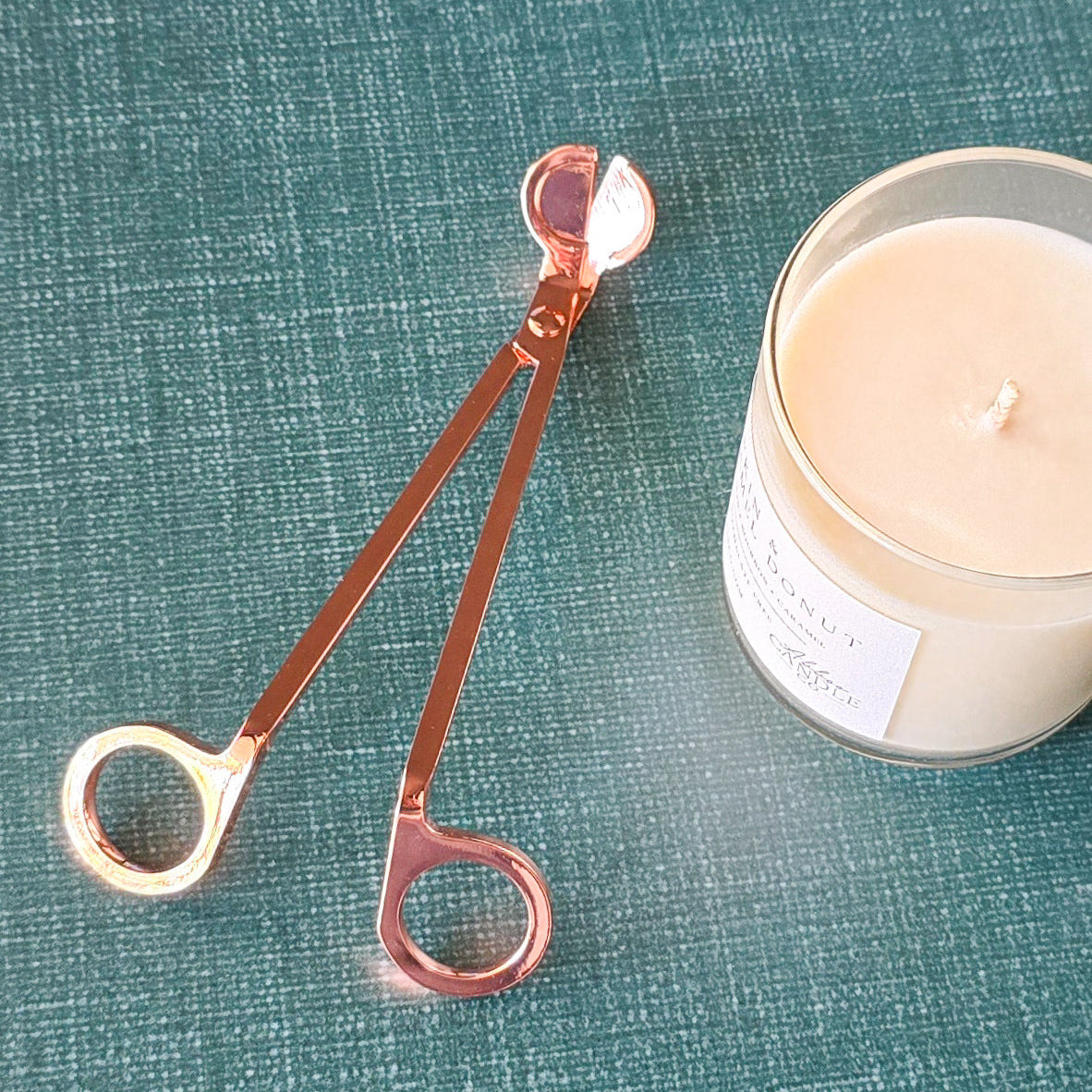 Rose Gold colored wick trimmer with a candle on green background