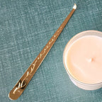 Gold-colored metal tool with engraved design next to a candle on a textured green surface