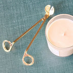 Gold candle wick trimmer on a green fabric background with a candle.