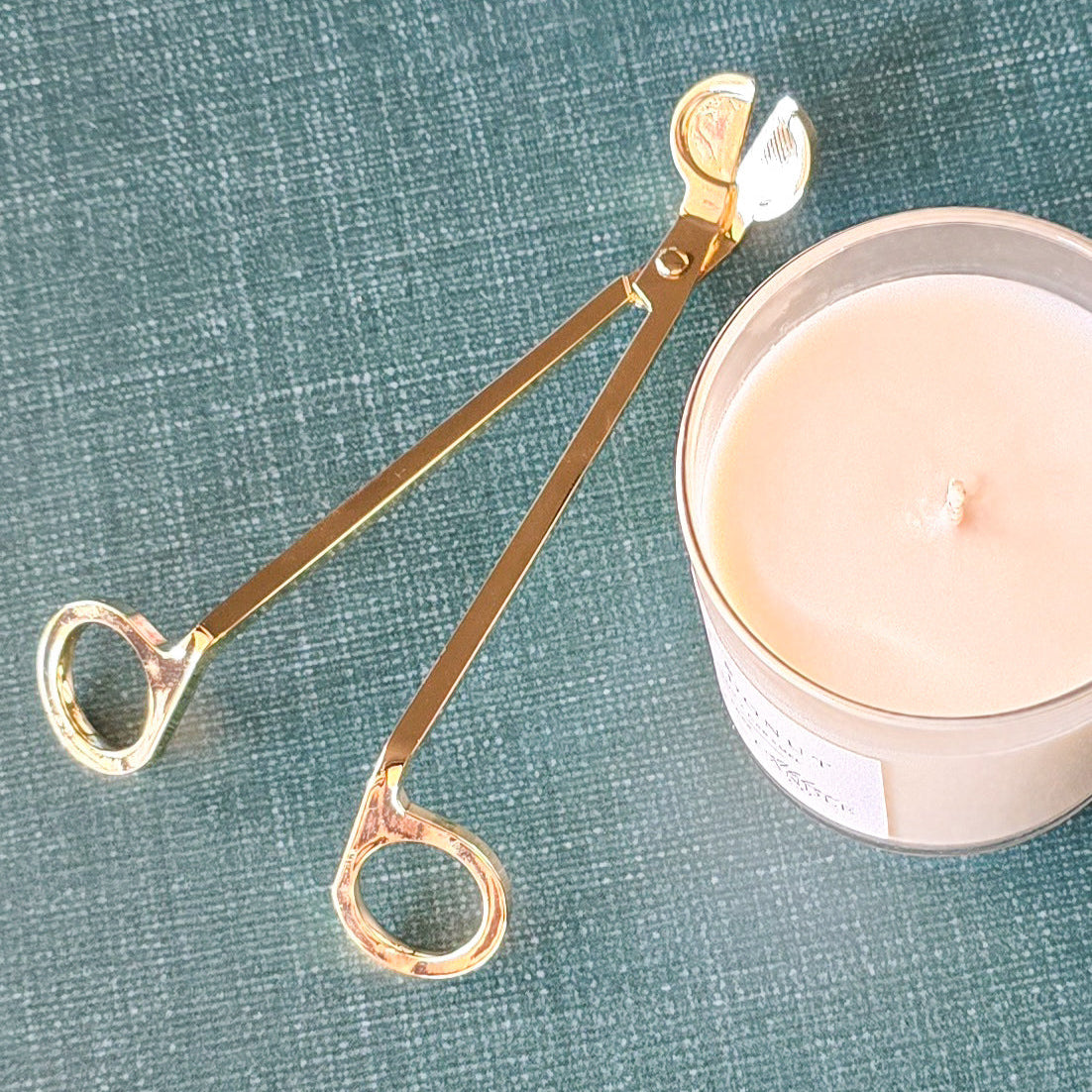 Gold candle wick trimmer on a green fabric background with a candle.