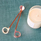 Rose Gold colored wick trimmer with a candle on green background