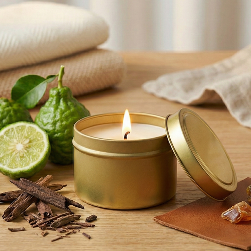 Gold candle in a tin with lit wick, surrounded by green fruit, mahogany wood, and lime on a wooden surface