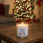 Candle with a Christmas-themed label on a table in front of a decorated Christmas tree.