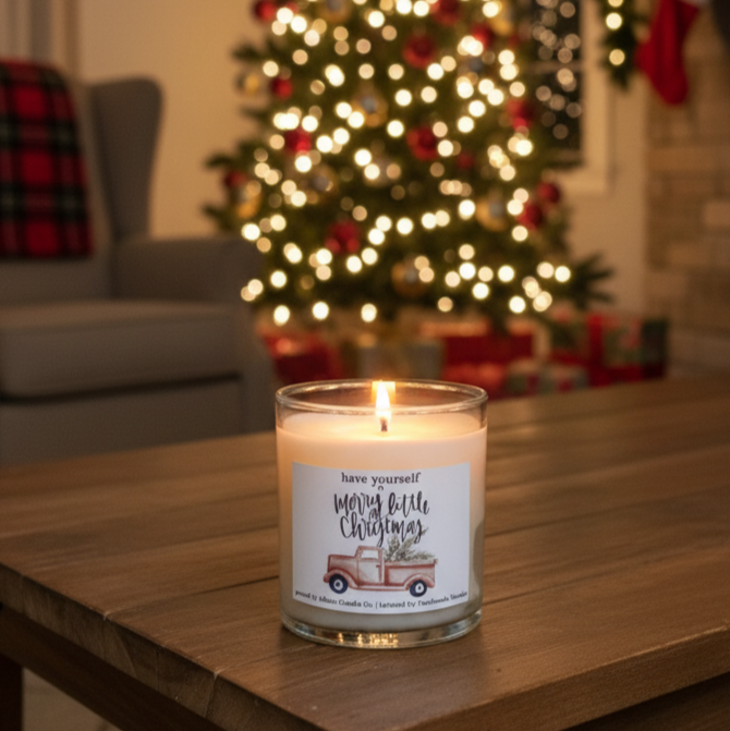 Candle with a Christmas-themed label on a table in front of a decorated Christmas tree.