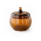 An amber glass pumpkin-shaped lidded candle with a ribbed design and a small stem, shown on a plain white background.