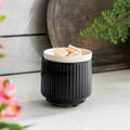 Black ribbed wax melt warmer with a white lid holding small objects on a light surface with blurred background