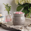 Gray ceramic wax warmer with pink wax melts on a table with flowers and books in the background
