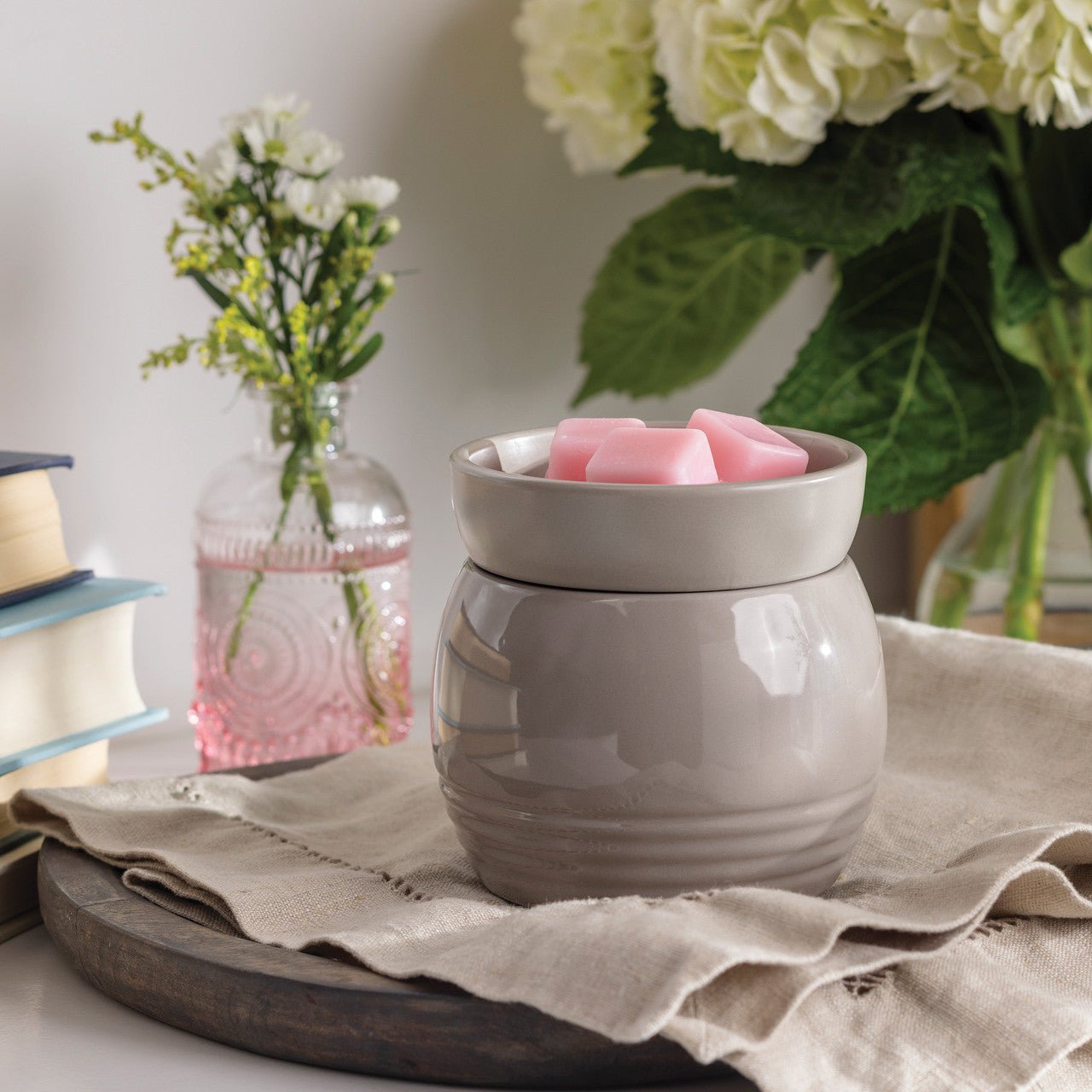 Gray ceramic wax warmer with pink wax melts on a table with flowers and books in the background