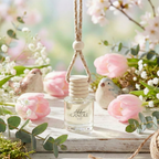 A bottle of Abboo Candle Co. hanging car diffuser on a wooden surface with pink flowers and greenery.